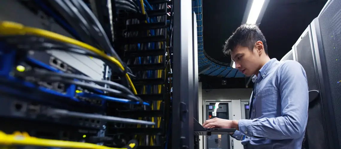 Telecom network engineer at server rack Network engineer working at a data centre server rack with blue and yellow fibre cabling