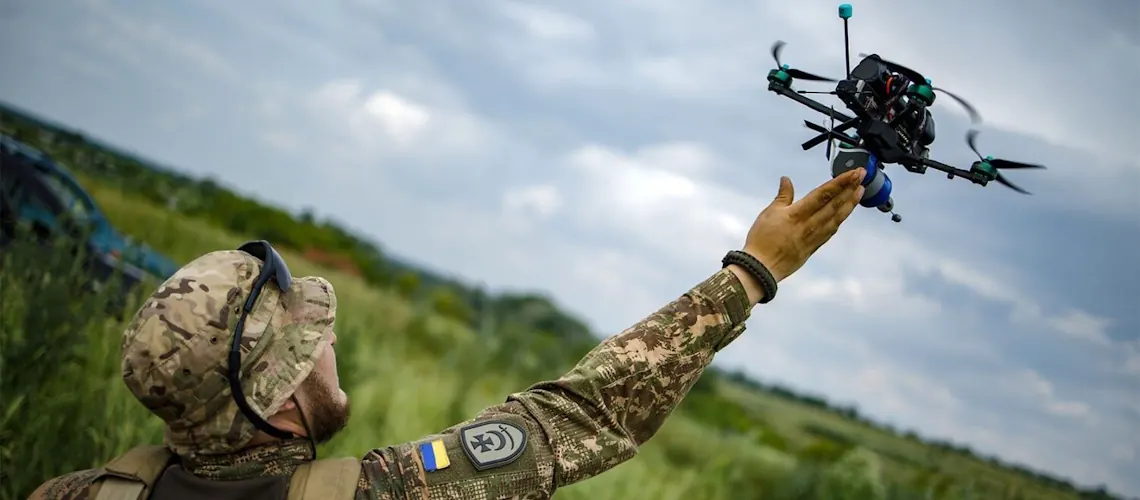 Drone operator launching an uncrewed aerial system Soldier in camouflage launching a small quadcopter drone by hand in an open field